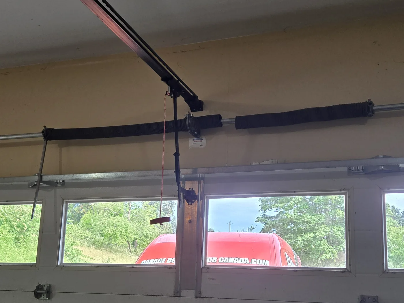 Broken torsion spring above a double garage door at a home near Holland Creek in Ladysmith, with the Garage Door Doctor Canada van visible through the door windows