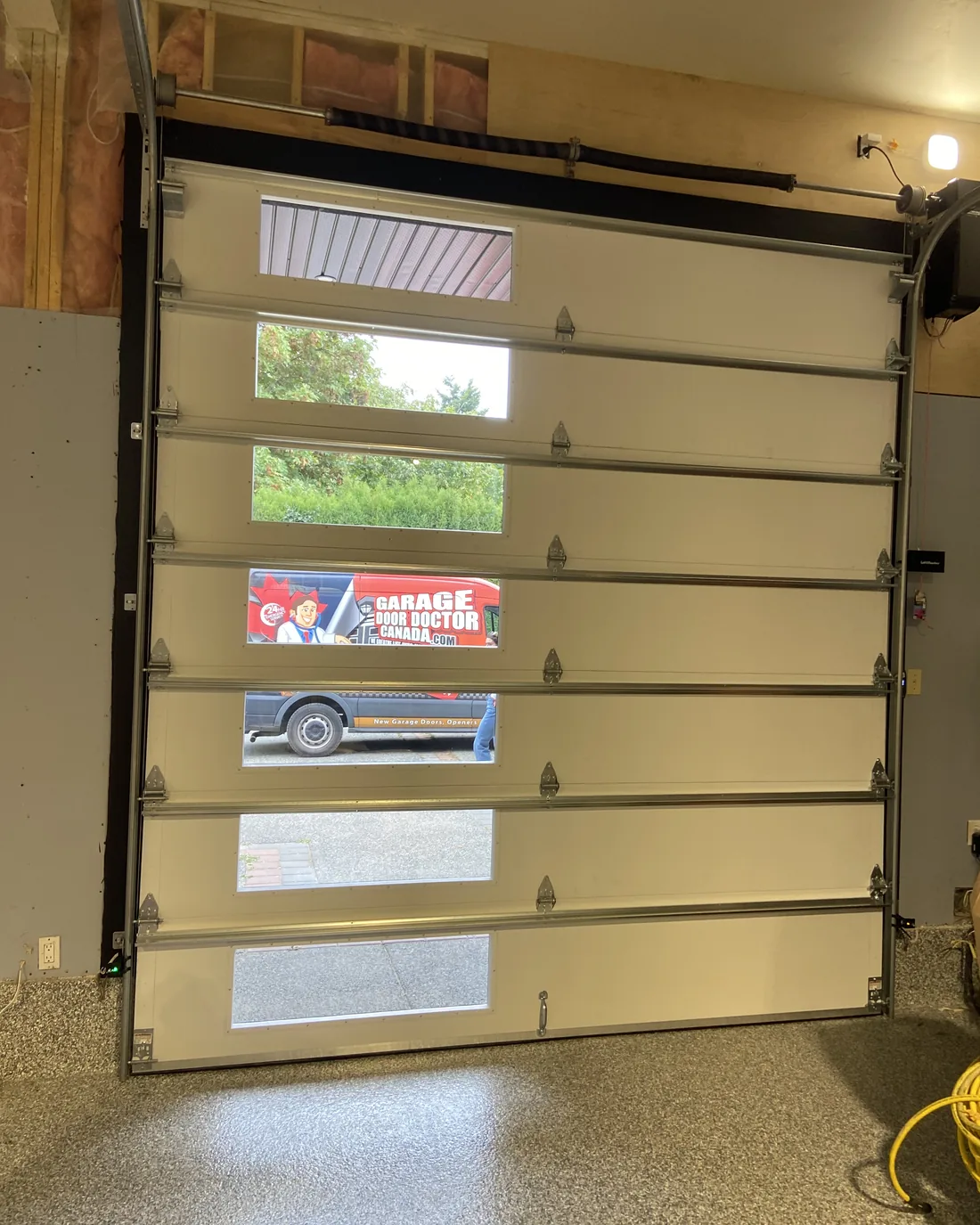 Inside view of the same Therma Tech 3400 door in a Departure Bay workshop, daylight coming through the glazing with the Garage Door Doctor Canada van outside
