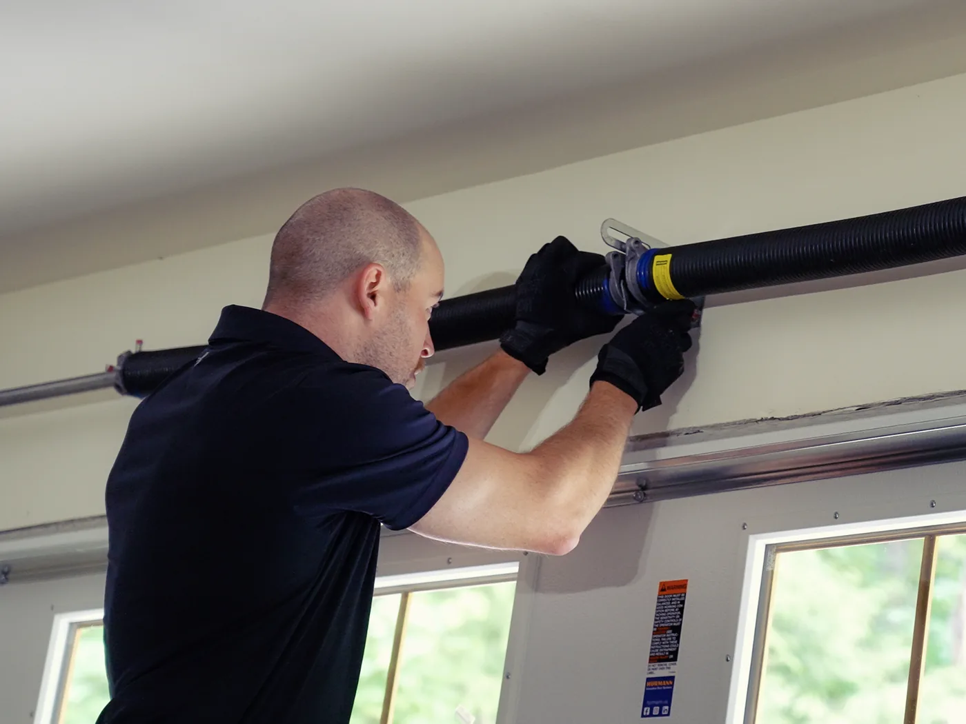 Caleb, co-owner of Garage Door Doctor Canada, winding a torsion spring above a garage door during a spring replacement